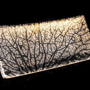 May include: A black rectangular serving tray with a white leaf pattern. The tray is made of glass and has a slightly curved shape.