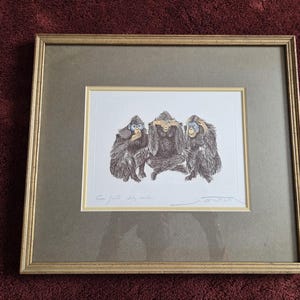 May include: Framed artwork featuring three monkeys in a 'see no evil, hear no evil, speak no evil' pose. The monkeys are depicted in a detailed, illustrative style with brown fur and blue accents. The artwork is framed in a gold-toned frame.