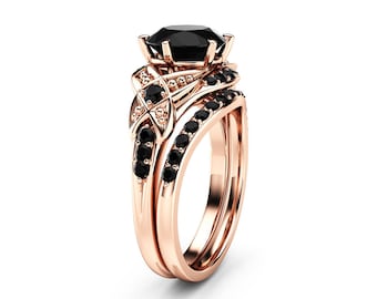 May include: Rose gold engagement ring set with a large, faceted black gemstone and smaller black stones. The band features intricate detailing and a matching wedding band. The ring is set against a white background.