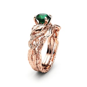 Puede incluir: Un anillo de compromiso de oro rosa con una esmeralda verde engastada en un dise&ntilde;o de rama retorcida.