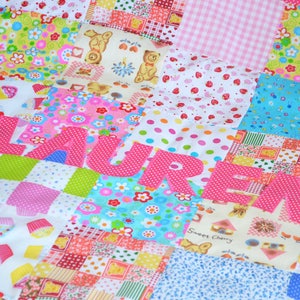 May include: A colorful patchwork quilt with the name "LAUREN" appliqu&eacute;d in pink polka dot fabric. The quilt features various patterned squares with floral, cupcake, and teddy bear designs. The color palette includes pink, blue, green, and white.