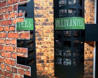May include: A miniature model of a brick building with two storefronts. The storefront on the left says "TIERS" and the storefront on the right says "OLLIVANDER'S".