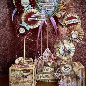 Può includere: Un set di sei decorazioni natalizie in stile vintage, ognuna con un design diverso. Le decorazioni sono realizzate in carta e hanno un aspetto rustico e fatto a mano. Le decorazioni sono disposte su un tavolo con uno sfondo di glitter rosso. Le decorazioni includono un ventaglio di carta rosso e bianco con una nota musicale, un ventaglio di carta verde e bianco con il testo "Oh Christmas Tree", un ventaglio di carta rosso e bianco con il testo "We Wish You A Merry Christmas", un ventaglio di carta rosso e bianco con il testo "Oh, Holy Night", un ventaglio di carta bianco con il testo "White Christmas", e un ventaglio di carta marrone con il testo "Jingle Bells".