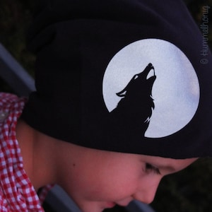 Könnte beinhalten: Eine schwarze Mütze mit einem weißen Wolf, der zum Mond heult. Die Mütze wird von einem Kind getragen.
