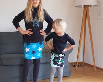 May include: Two girls wearing skirts with different patterns. The girl on the left is wearing a blue skirt with white stars. The girl on the right is wearing a green and pink skirt with a floral pattern.