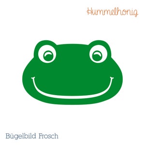 Könnte beinhalten: Grüner Froschgesichts-Bügeleisen mit einem lächelnden Mund und weißen Augen. Der Patch ist mit "Bügelbild Frosch" beschriftet, was "Bügeleisen-Frosch" bedeutet.