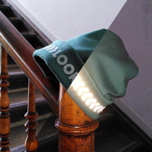 Könnte beinhalten: Eine grüne Mütze mit einem reflektierenden Streifen und dem Wort "LOOK" auf der Seite.