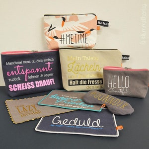 Könnte beinhalten: Eine Sammlung von neun kleinen Reißverschlusstaschen mit verschiedenen Sprüchen und Designs. Die Taschen sind aus weichem, strukturiertem Stoff und haben eine Vielzahl von Farben, darunter Schwarz, Grau, Pink und Türkis. Die Sprüche auf den Taschen lauten: "#MeTime", "Mein Talent: Lächeln", "Manchmal muss man einfach entspannen, sich zurücklehnen und sagen: Scheiß drauf!" "Innerer Frieden", "Hallo Schön", "Geduld ist nicht meine Stärke", "Ich bin nicht faul, ich mache einfach nichts!" und "Komm schon, ich habe nicht ewig Zeit".