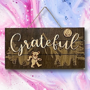 May include: A wooden sign with the word "Grateful" in cursive script, a dancing bear, and a mountain scene. The sign has a distressed wood look and is hanging from a rope.