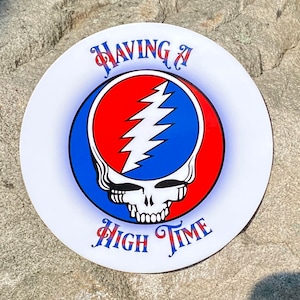May include: A white round sticker with a blue and red Grateful Dead Steal Your Face logo. The text "HAVING A HIGH TIME" is written in a stylized font.