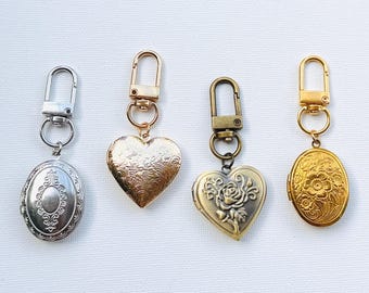 Könnte beinhalten: Vier Metallmedaillons mit Schlüsselanhängern. Die Medaillons sind in Silber-, Gold- und Bronzetönen gehalten und haben ovale und herzförmige Formen. Das ovale Medaillon hat ein verziertes Design, während die herzförmigen Medaillons florale und geprägte Muster aufweisen.