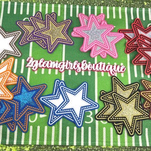 May include: A collection of star-shaped embellishments in various colors, including brown, purple, pink, red, orange, blue, and gold. Each star has a white center and a dotted border. The text "2glamgirls boutique" is visible.