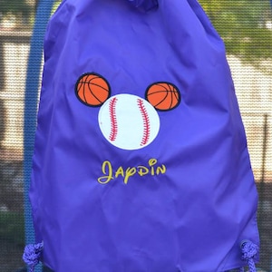 May include: Purple drawstring bag with a baseball and basketball design. The bag has the name "Jappdin" embroidered on it in yellow.