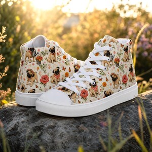 May include: A pair of high-top canvas sneakers featuring a cream-colored background with a repeating pattern of pugs, red roses, orange marigolds, and small butterflies. The shoes have white rubber toe caps, white laces, and white rubber soles.