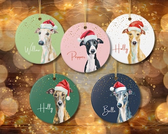 May include: Five round Christmas ornaments featuring whippet dog portraits wearing Santa hats. Each ornament has a different background color: green, pink, white, dark green, and navy blue. Each ornament has a dog's name written on it.