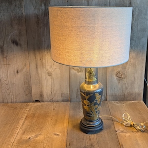 May include: A gray ceramic table lamp with a gold floral design on the base. The lamp has a white fabric shade.