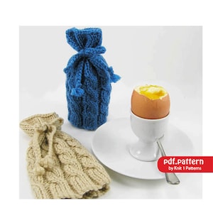 May include: A blue and tan knitted egg cozy and a blue knitted bottle cozy. A soft-boiled egg sits in a white egg cup on a white plate. The image includes the text "pdf.pattern by Knit 1 Patterns".
