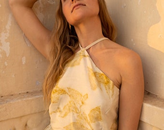 May include: A woman wearing a halter top and matching skirt with a leaf print in shades of yellow and cream. The top is tied at the neck and the skirt has a drawstring waist.