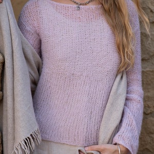 May include: A pale pink, lightweight knit sweater with a loose fit and long sleeves. The sweater is made of a delicate, open-weave fabric.