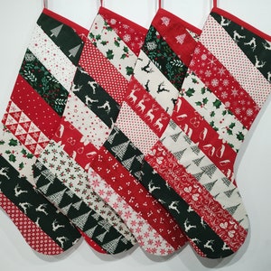 Pode incluir: Quatro meias de Natal vermelhas e verdes com um design de patchwork. Cada meia é feita de tecidos diferentes com vários padrões natalinos, incluindo renas, árvores, azevinho e flocos de neve.