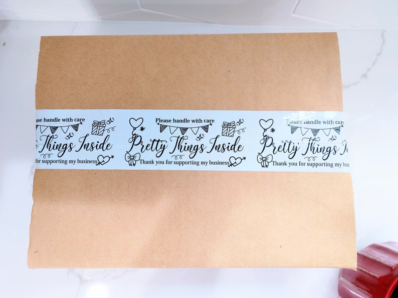 Puede incluir: Una caja de cart&oacute;n marr&oacute;n con una etiqueta de cinta blanca y azul que dice "Por favor, manipule con cuidado Pretty Things Inside Gracias por apoyar mi negocio".