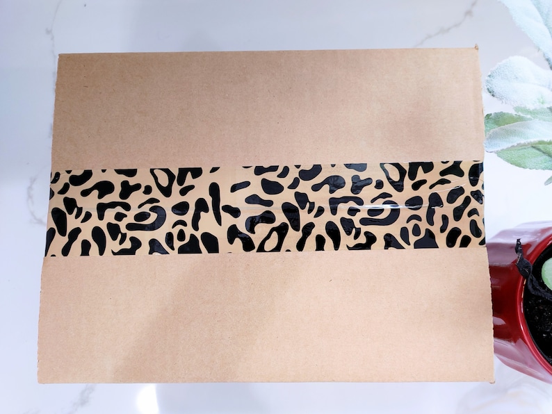 Puede incluir: Un paquete de papel marr&oacute;n con una cinta de estampado de leopardo negro y marr&oacute;n en el medio.