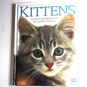 May include: A book titled "KITTENS" features a close-up of a kitten's face with green eyes and gray and brown fur. The text below the title reads "An ideal introduction to the world of kittens."