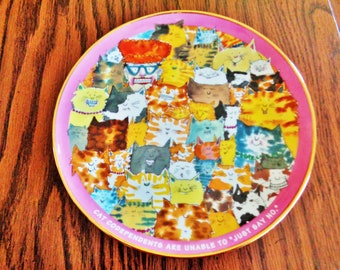 May include: A decorative plate with a pink rim and gold trim, featuring a colorful illustration of numerous cartoon cats. The cats have various expressions and colors. The plate has the text "CAT CODEPENDENTS ARE UNABLE TO 'JUST SAY NO.'"