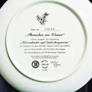 May include: White ceramic plate with text in German, including "Planschen am Wasser" and "Katzenkinder auf Entdeckungsreise." Features a floral design and the Bradex and Kahla logos. The plate is a limited edition.