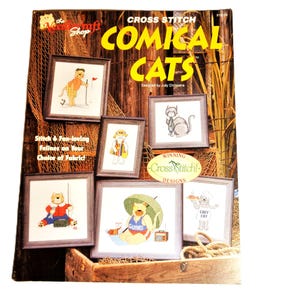 May include: A book cover titled "CROSS STITCH COMICAL CATS" featuring framed cross-stitch designs of cats in various humorous scenarios. The cover includes text such as "Stitch & Fun-loving Fellines on Your Choice of Fabric!" and "Winning Cross Stitch! Designs."