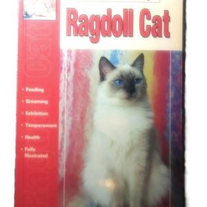 May include: A book titled "The Guide to Owning a Ragdoll Cat" features a Ragdoll cat with blue eyes. The cover has a red spine with the word "Cat" vertically. Topics include feeding, grooming, and health.