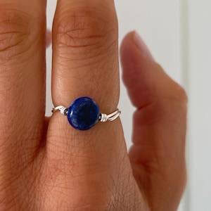 May include: A silver wire wrapped ring with a round blue lapis lazuli gemstone.
