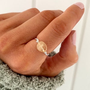 May include: A silver ring featuring a clear, pale yellow gemstone. The ring is wrapped in silver wire.
