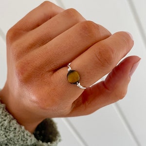 May include: A silver ring with a round, brown and gold gemstone. The ring is on a person's finger.