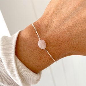 Könnte beinhalten: Ein zartes Armband aus silberner Kette mit einem einzigen, hellrosa ovalen Edelstein.