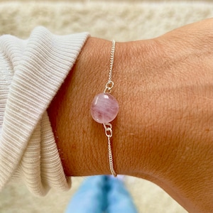 May include: A delicate silver chain bracelet with a single round pink gemstone charm.