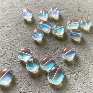 May include: A collection of iridescent oval-shaped glass beads. The beads have a rainbow effect and are translucent.