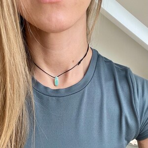 May include: A simple necklace with a light blue gemstone pendant on a black cord.