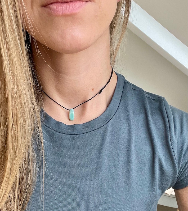May include: A simple necklace with a light blue gemstone pendant on a black cord.