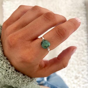 May include: A silver ring with a green gemstone. The ring is on a finger.