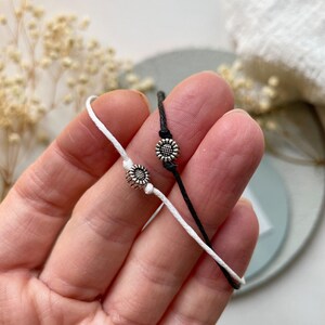 Peut inclure: Deux bracelets d'amiti&eacute;, un blanc et un noir, chacun orn&eacute; d'un petit charm en forme de tournesol argent&eacute;. Les bracelets sont en cordon et pr&eacute;sent&eacute;s sur un fond doux et neutre. Les breloques tournesol ajoutent une touche d&eacute;licate.