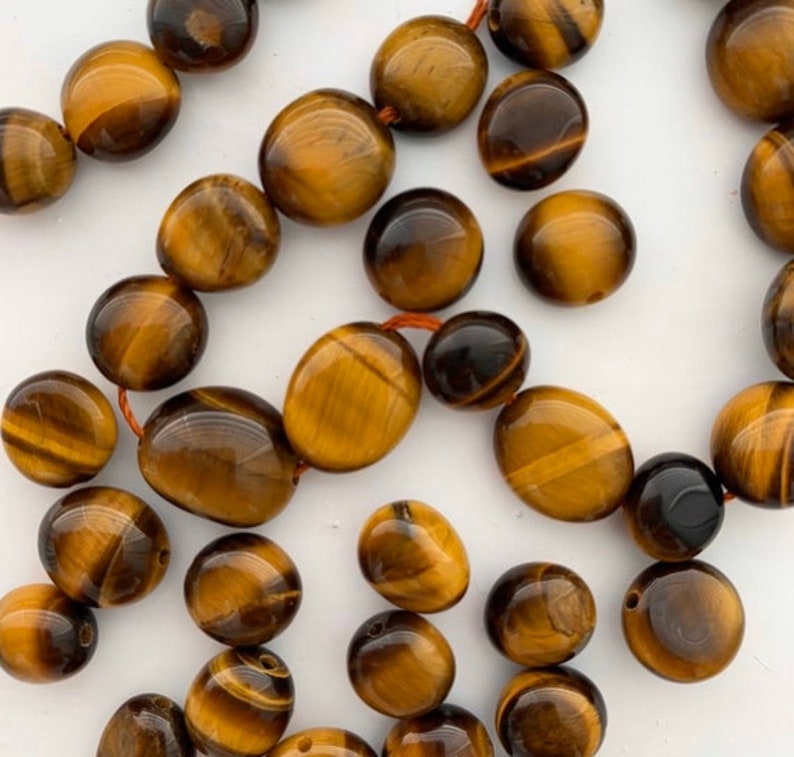 May include: A strand of tiger's eye beads, each bead is a smooth, oval shape with a golden brown color and a shimmering, chatoyant effect.