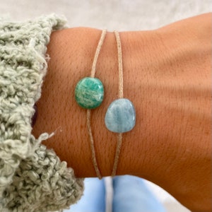 Könnte beinhalten: Ein schlichtes Armband mit zwei natürlichen Steinperlen. Das Armband besteht aus einem hellbraunen Band und hat eine grüne Aventurinperle und eine hellblaue Aquamarinperle.
