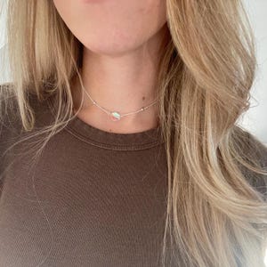 May include: A silver chain choker necklace with a small iridescent charm.