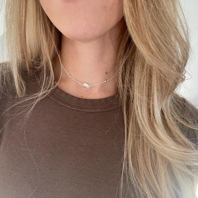 May include: A silver chain choker necklace with a small iridescent charm.
