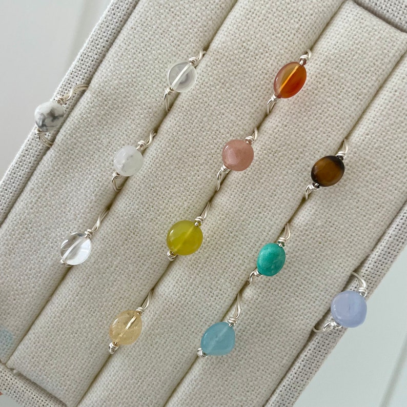 May include: A set of ten silver rings with different colored gemstone beads. The rings are displayed in a white fabric-lined box.