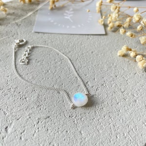 May include: A silver chain bracelet with a round, iridescent moonstone charm.