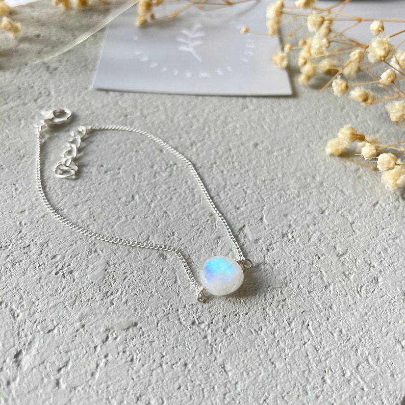 May include: A silver chain bracelet with a round, iridescent moonstone charm.