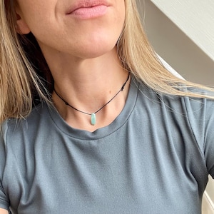 May include: A simple, minimalist necklace with a light blue oval pendant on a black cord.