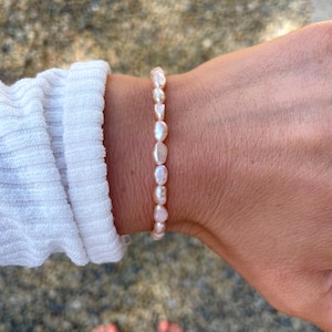 May include: A delicate bracelet made of a string of pale pink freshwater pearls. The pearls are irregularly shaped and have a natural, organic look.